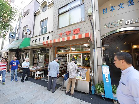 Foto einer Einkaufsstraße mit drei Buchhandlungen und Passanten. Schriftzeichen der Läden japanisch.